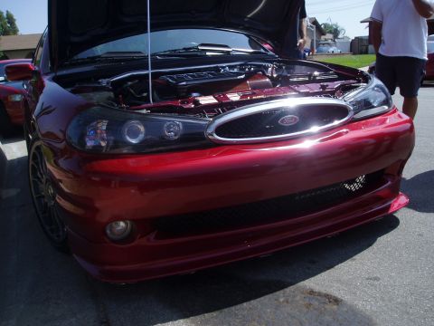 1993 Ford Taurus - A red Ford sedan with its hood open reveals the engine and custom details, including aftermarket headlights and grille.