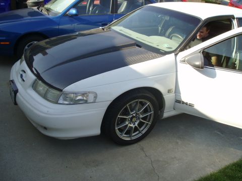 1993 Ford Taurus - This white sedan features a contrasting black hood and aftermarket wheels, seen from a 3/4 front angle.