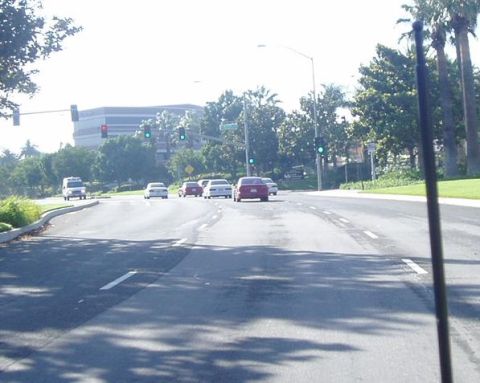 1993 Ford Taurus - Multiple vehicles are seen driving on a road with traffic lights and trees lining the sides.