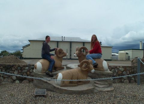 1996 Ford Bronco - Two women pose atop bighorn sheep statues, with a building and cloudy sky in the background.