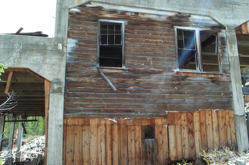Abandoned wooden building with two broken windows and concrete supports