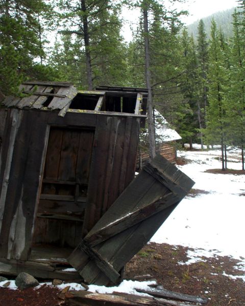 1996 Ford Bronco - An old, weathered outhouse stands in a wooded area with snow on the ground, its roof and door in disrepair.