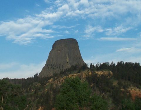 1996 Ford Bronco - Devils Tower National Monument, a prominent geological formation, is seen against a backdrop of trees and a partly cloudy sky.