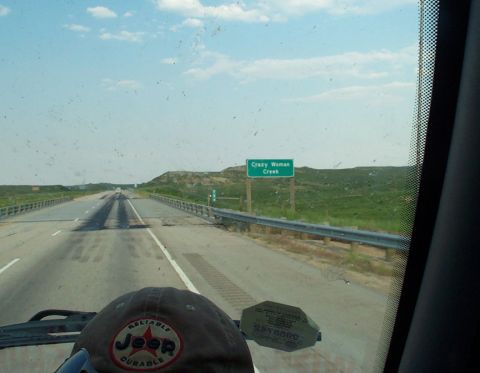 1996 Ford Bronco - Driving down a highway with a sign indicating Crazy Woman Creek, under a partly cloudy sky.