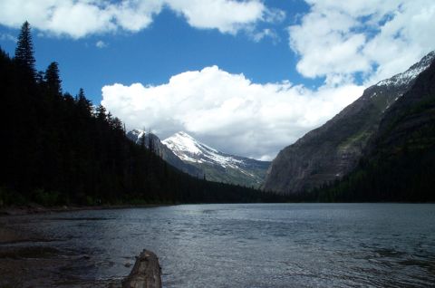 1996 Ford Bronco - A lake is surrounded by dark forests and snow-capped mountains under a partly cloudy sky.