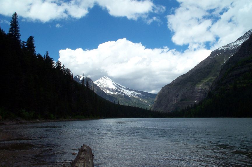 Lake with mountains and trees under a cloudy sky. Supermotors.net logo in corner