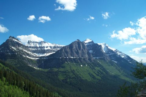 1996 Ford Bronco - A scenic view of mountains with snow-covered peaks and lush green slopes, set against a bright blue sky with scattered clouds.