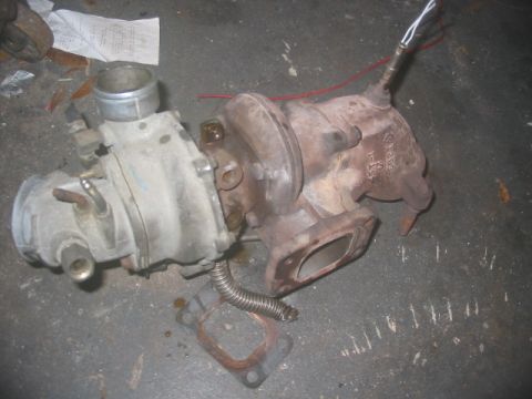 1985 Ford LTD Crown Victoria - A turbocharger assembly, likely removed from a vehicle, rests on a concrete surface.