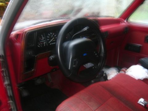 1989 Ford Bronco II - The interior of a vehicle shows the dashboard, steering wheel, and red seats.
