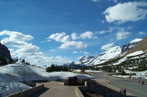 1996 Ford Bronco - A scenic mountain road winds through snow-covered terrain under a bright blue sky with scattered clouds.