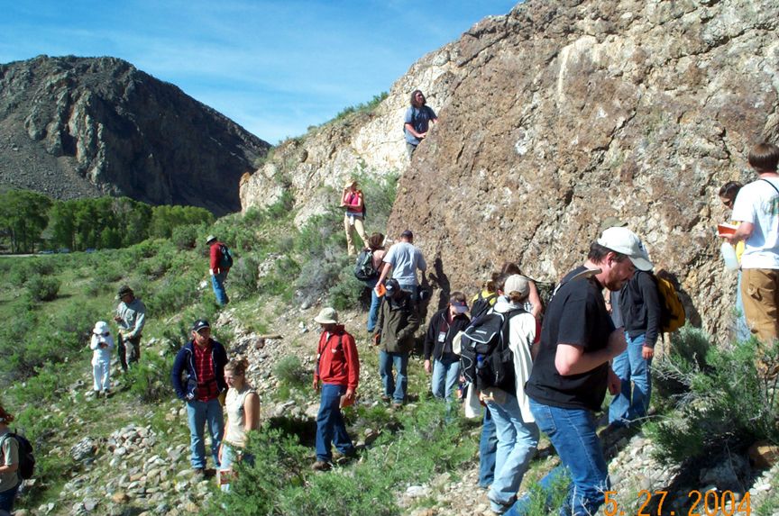 Group of people hiking on a rocky hillside with sparse vegetation and mountains in the background