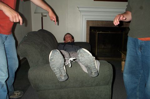 1996 Ford Bronco - A man is tied to a chair as two individuals point at him, with a fireplace in the background.