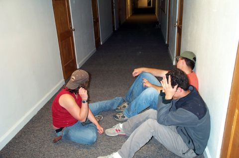 1996 Ford Bronco - Three individuals are seated on the floor of a long, carpeted hallway, with wooden doors lining the walls.