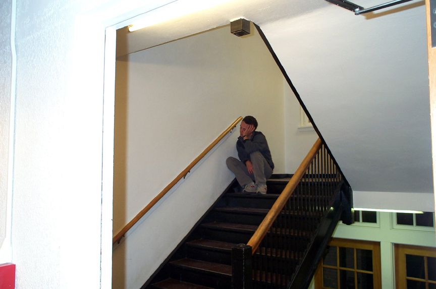 Person sitting on a dark wooden staircase, looking thoughtful
