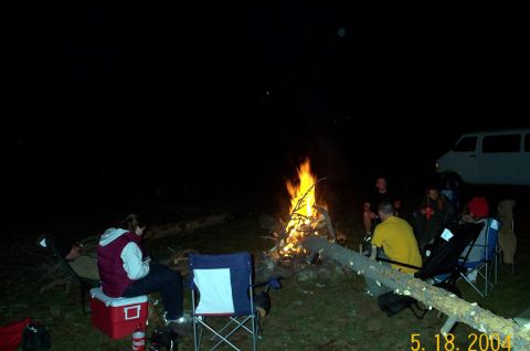 1996 Ford Bronco - A group of people gather around a campfire at night, with a white van visible in the background.