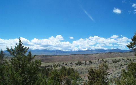 1996 Ford Bronco - A vast desert landscape stretches towards distant, snow-capped mountains under a bright, cloudy sky.