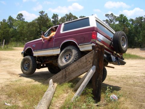 1990 Ford Bronco - A maroon and white Ford Bronco navigates an off-road obstacle course.