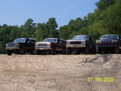 1987 Ford Bronco - A group of four SUVs, including a 1987 Ford Bronco, are parked on a dirt hill on a sunny day.