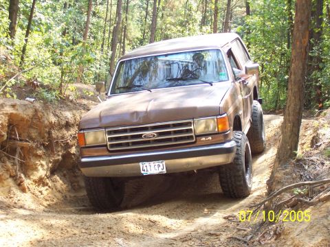 1987 Ford Bronco - A brown 1987 Ford Bronco navigates a challenging off-road trail with steep inclines.