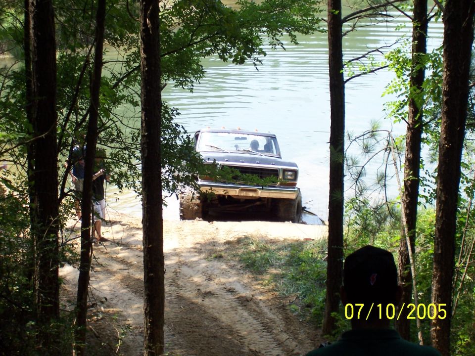 Black Ford Bronco driving into a lake, seen through trees