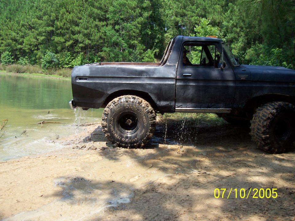 Side view of a black 1978 Ford Bronco with large tires, partially in water