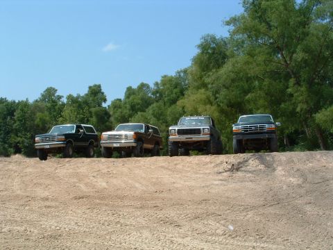 1993 Ford Bronco - Four Ford Broncos are lined up on a dirt embankment with trees in the background.