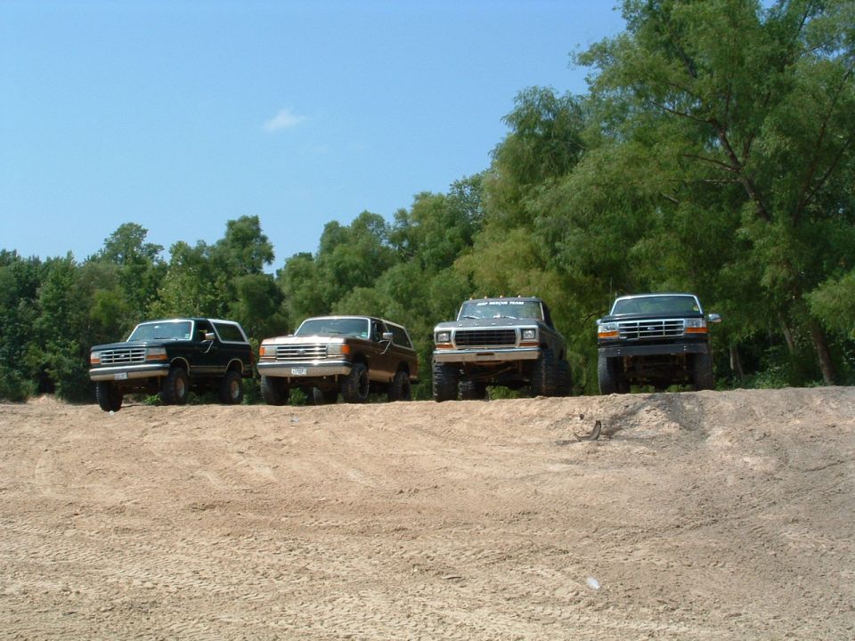Four Ford Broncos parked on a dirt berm under a blue sky