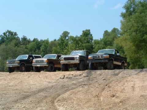 1993 Ford Bronco - Several Ford trucks and SUVs are lined up on a dirt embankment under a clear blue sky.