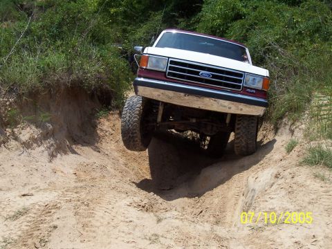 1987 Ford Bronco - A 1987 Ford Bronco navigates a steep, sandy trail with its front right wheel airborne.