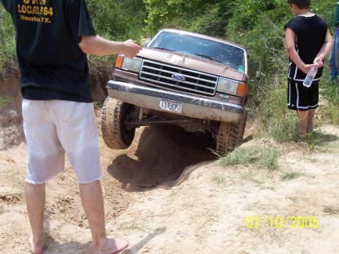 1987 Ford Bronco - A Ford Bronco navigates a challenging off-road obstacle with onlookers present.