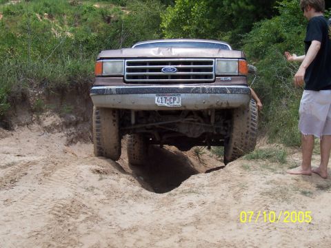 1987 Ford Bronco - A 1987 Ford Bronco navigates a challenging off-road terrain with a person observing.