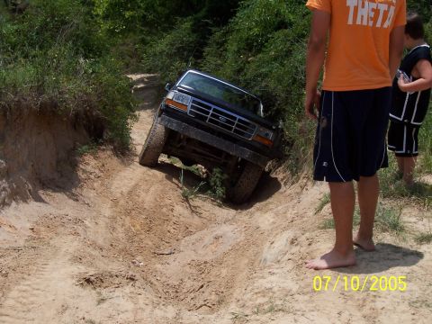 1987 Ford Bronco - A black Ford Bronco tackles a challenging off-road trail on a sunny day.