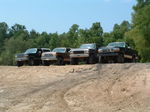 1993 Ford Bronco - A line of four Ford trucks are parked on a dirt embankment under a clear blue sky.