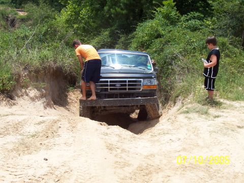 1987 Ford Bronco - A black Ford Bronco navigates a sandy off-road trail with two people nearby.