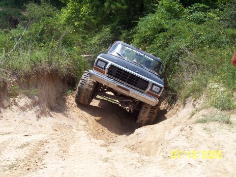 1987 Ford Bronco - This modified Ford Bronco is navigating a steep, sandy incline with large off-road tires.