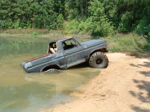 1993 Ford Bronco - This gray pickup truck, likely from the 1970s, is partially submerged in water with its large off-road tires visible.