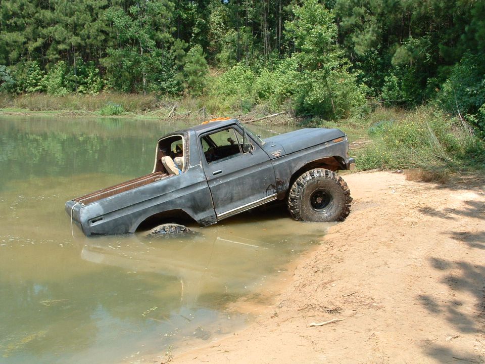Gray pickup truck with large tires partially submerged in water, 1970s body style