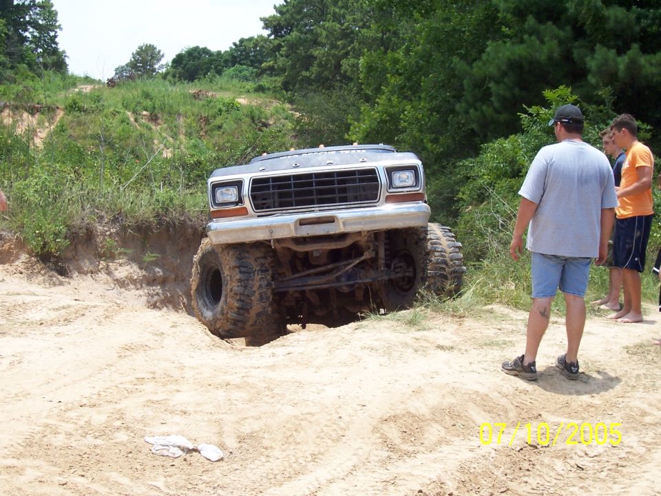 Modified 1978 Ford Bronco with large tires climbing a sandy incline, watched by three people