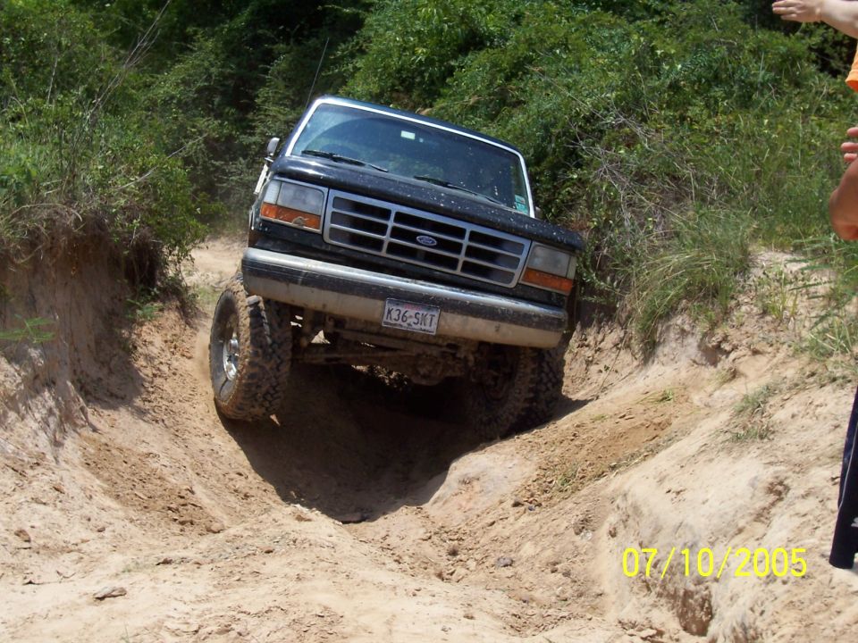 Black 1992 Ford Bronco with lifted suspension driving down a dirt path