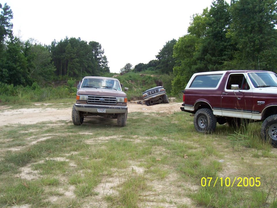 Maroon and white 1987 Ford Bronco parked on dirt with another Bronco and a truck in the background