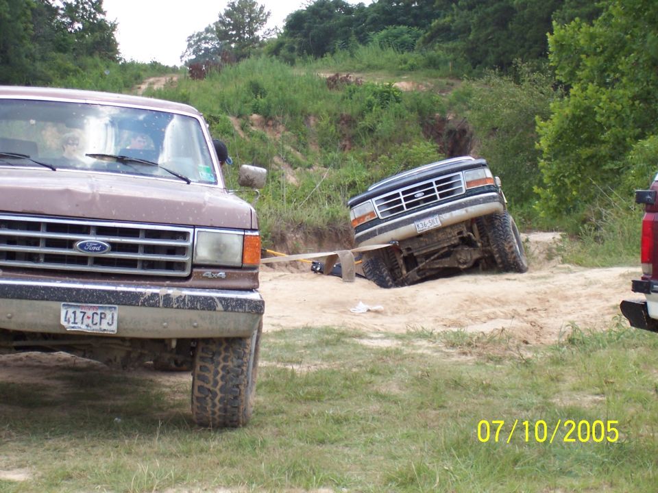 1987 Ford Bronco and another Ford truck on a dirt trail, one truck is tilted