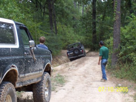1987 Ford Bronco - Two SUVs navigate a dirt path through a wooded area on a sunny day.