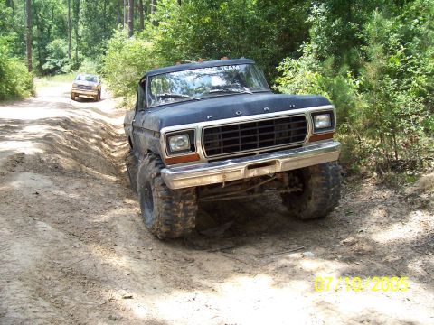 1987 Ford Bronco - A modified Ford truck navigates a dirt path with another vehicle in the background.