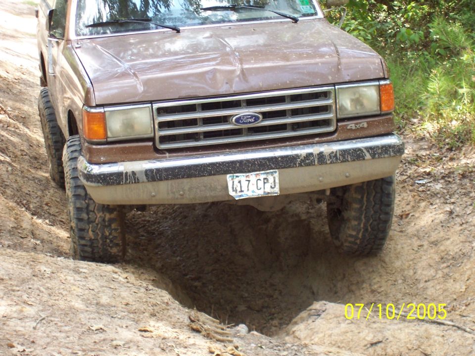 Brown Ford F-Series truck with a dented hood driving off-road