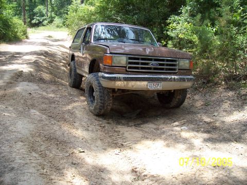 1987 Ford Bronco - A brown 1987 Ford Bronco is seen driving on a dirt path through a wooded area.