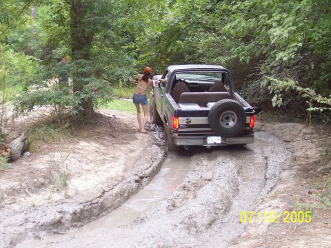 1987 Ford Bronco - A 1987 Ford Bronco tackles a challenging muddy path, with a woman leaning out the driver's side window.