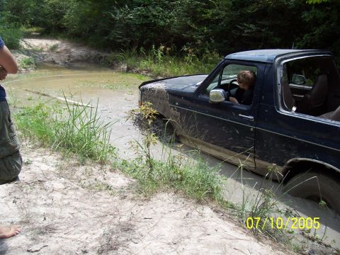 1987 Ford Bronco - A 1987 Ford Bronco is stuck in a muddy ditch with a person behind the wheel.