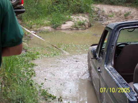 1987 Ford Bronco - A vehicle is stuck in a muddy water crossing, with another vehicle partially visible in the background.