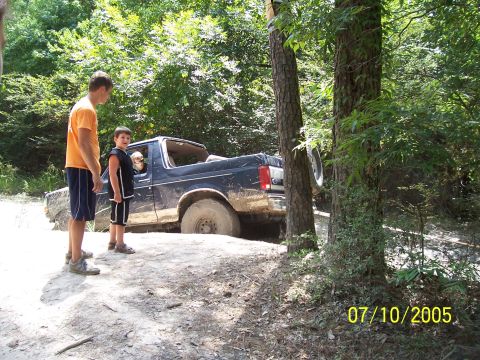 1987 Ford Bronco - A 1987 Ford Bronco is stuck in the mud with two people standing nearby.