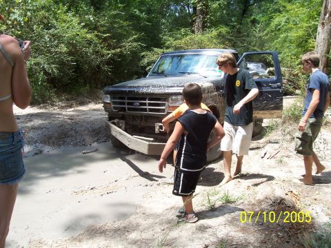 1987 Ford Bronco - People gather around a 1987 Ford Bronco stuck in a muddy area.
